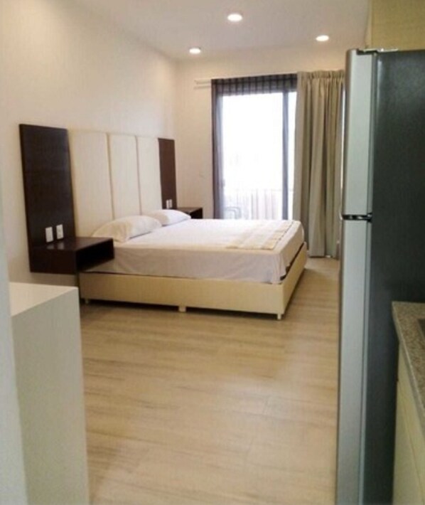 A bedroom with a bed, bedside tables, a wardrobe, a window with curtains, and a refrigerator.