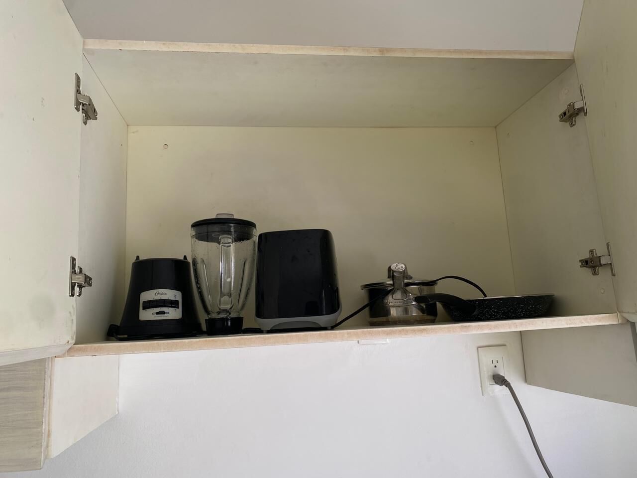 A kitchen with a blender, toaster, and a frying pan on the countertop.