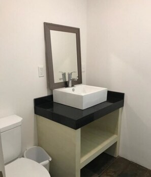 Un baño pequeño con lavamanos blanco, un espejo y un inodoro.
