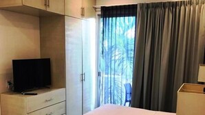 A hotel room with a large bed, a TV on a dresser, and a view of the outdoors through a window with curtains. - Estudio cerca del mar, en Puerto Aventuras 201 (Puerto Aventuras)