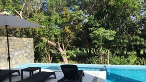 A poolside area with lounge chairs and a table, surrounded by a stone wall and lush greenery. - Estudio cerca del mar, en Puerto Aventuras 201 (Puerto Aventuras)