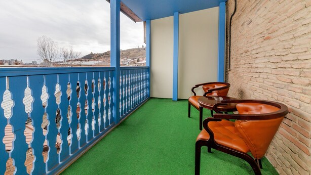 A balcony with green artificial grass, a blue railing with decorative elements, and a brick wall. - Hotel Marlyn (Tbilisi)