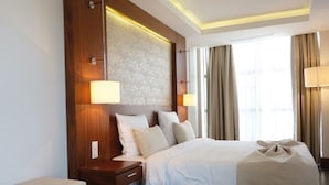 Een hotelkamer met een groot bed, een nachtkastje, een lamp en uitzicht op de stad door het raam.
