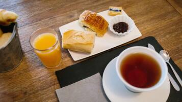A breakfast setting with pastries, a glass of orange juice, and a cup of tea on a wooden table.