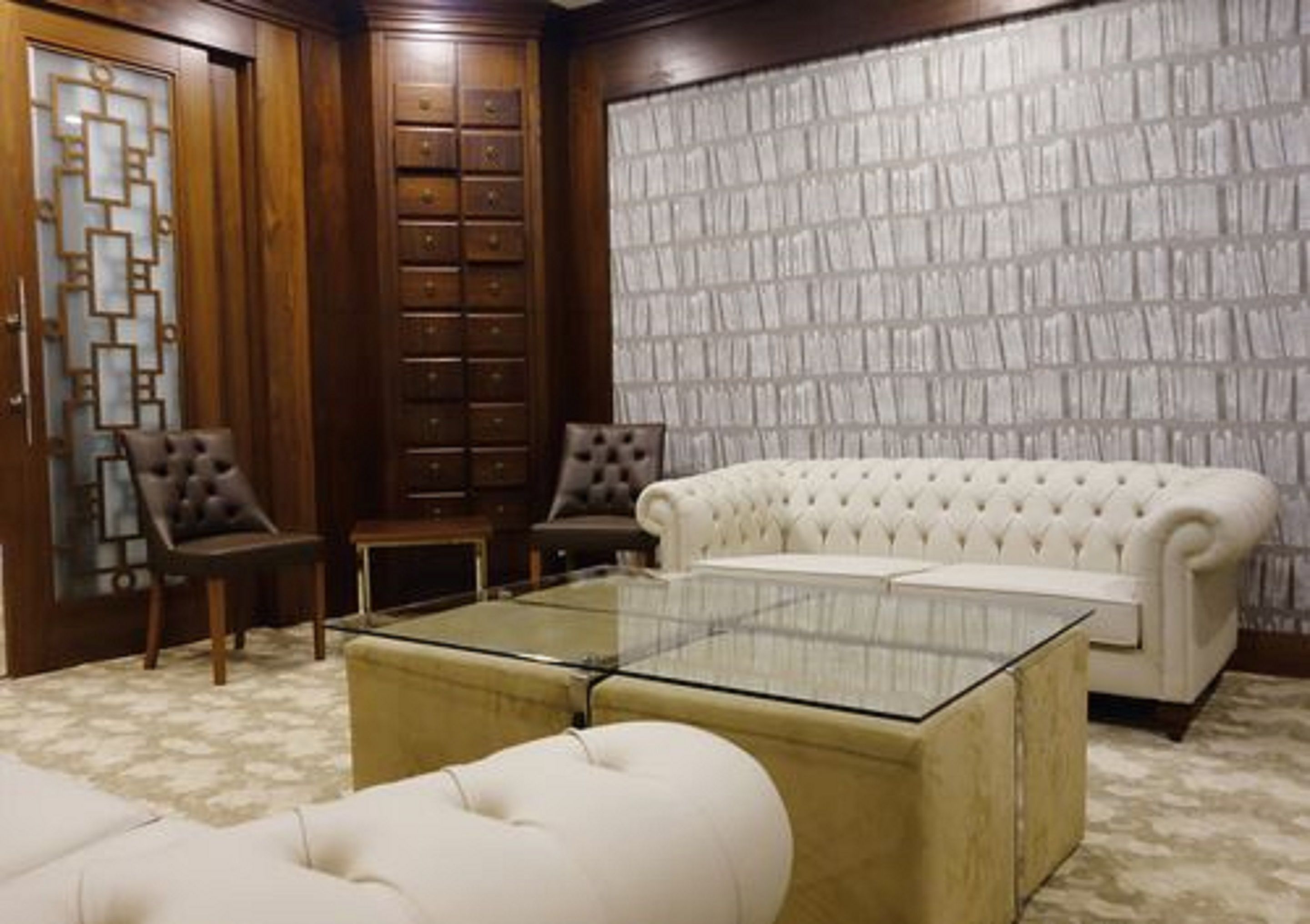 A room with a glass-top coffee table, a tufted sofa, and a patterned wallpaper wall.