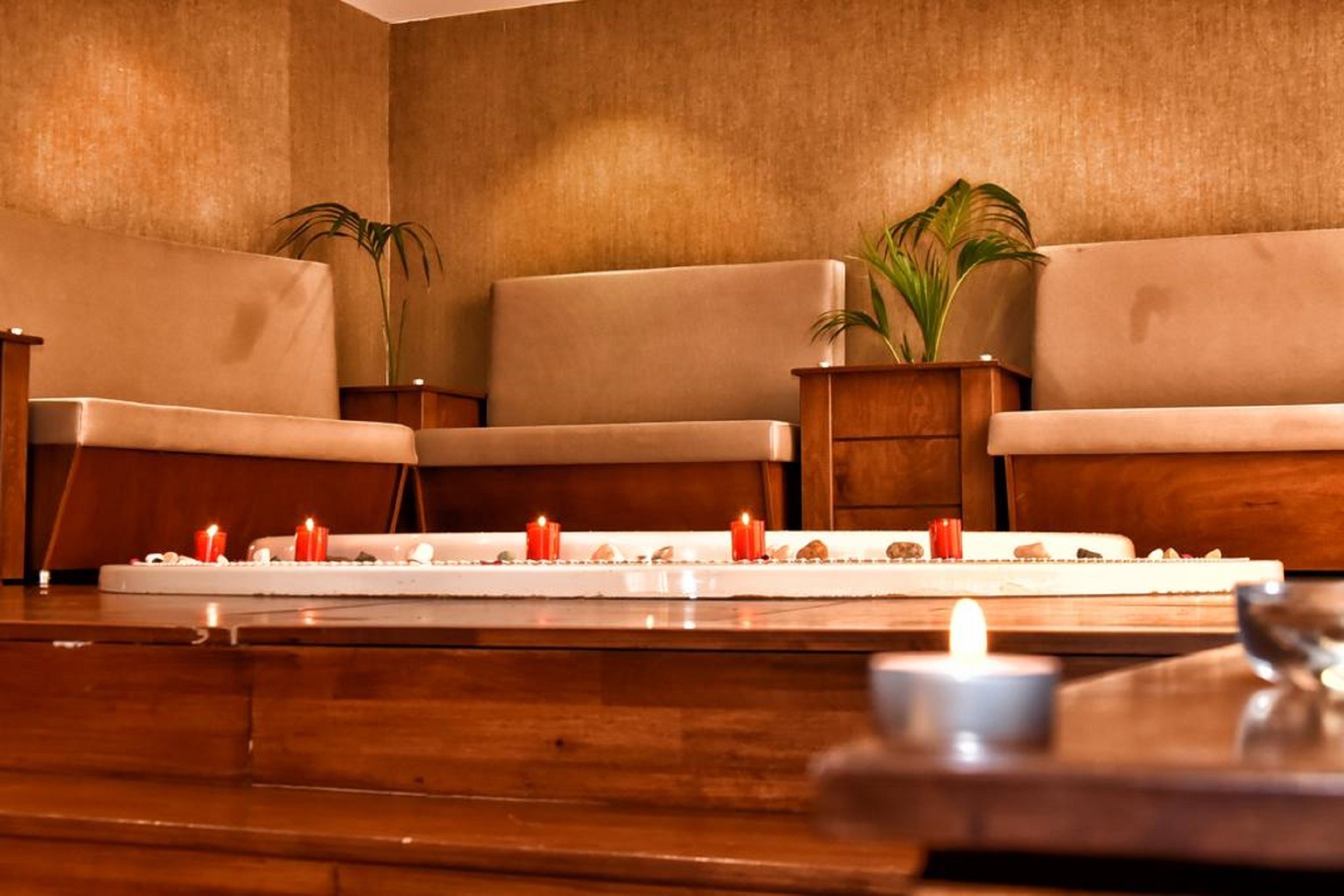 Une salle de spa avec trois canapés beiges, une table en bois et un petit autel orné de bougies.