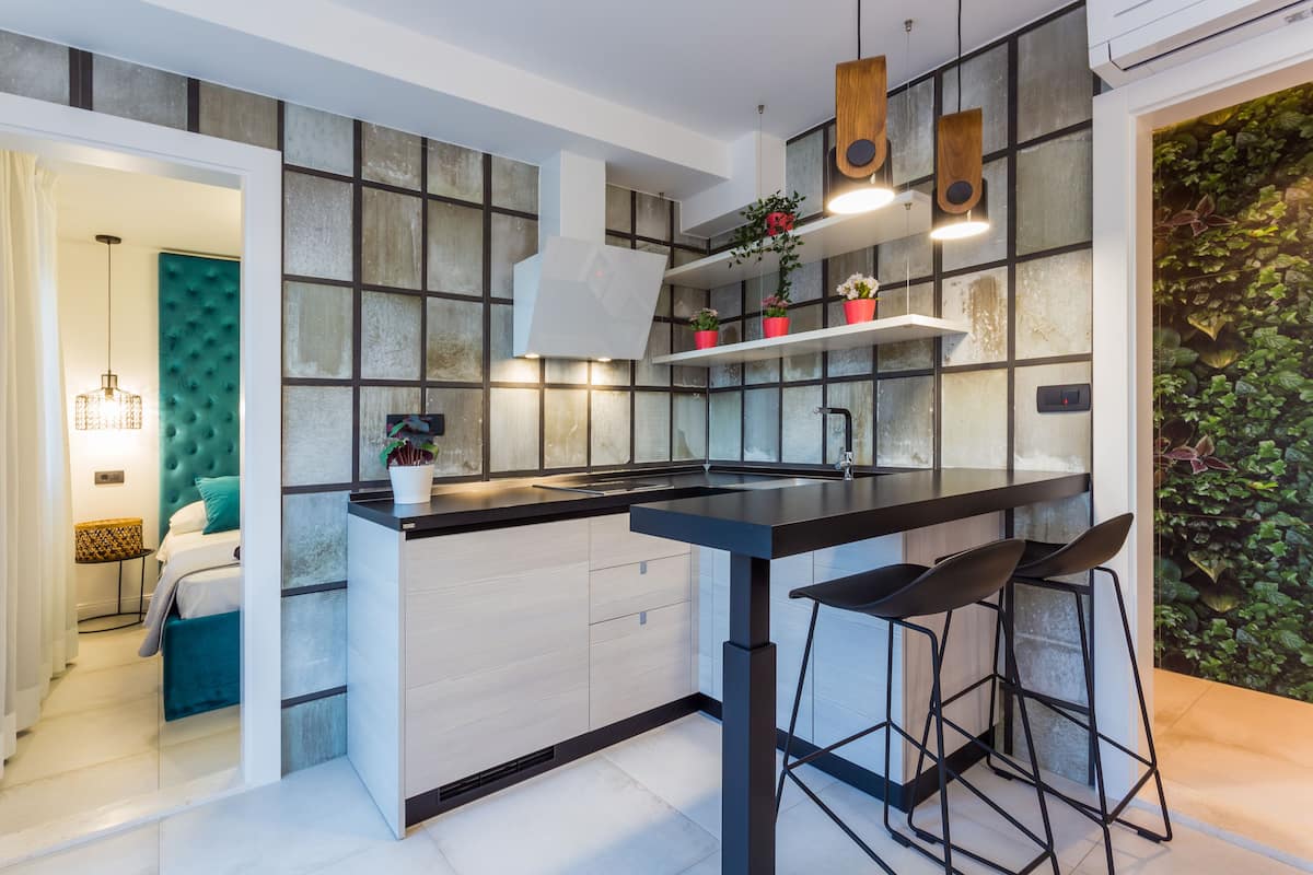 A modern kitchen with a central island, bar stools, and a green wall with plants.