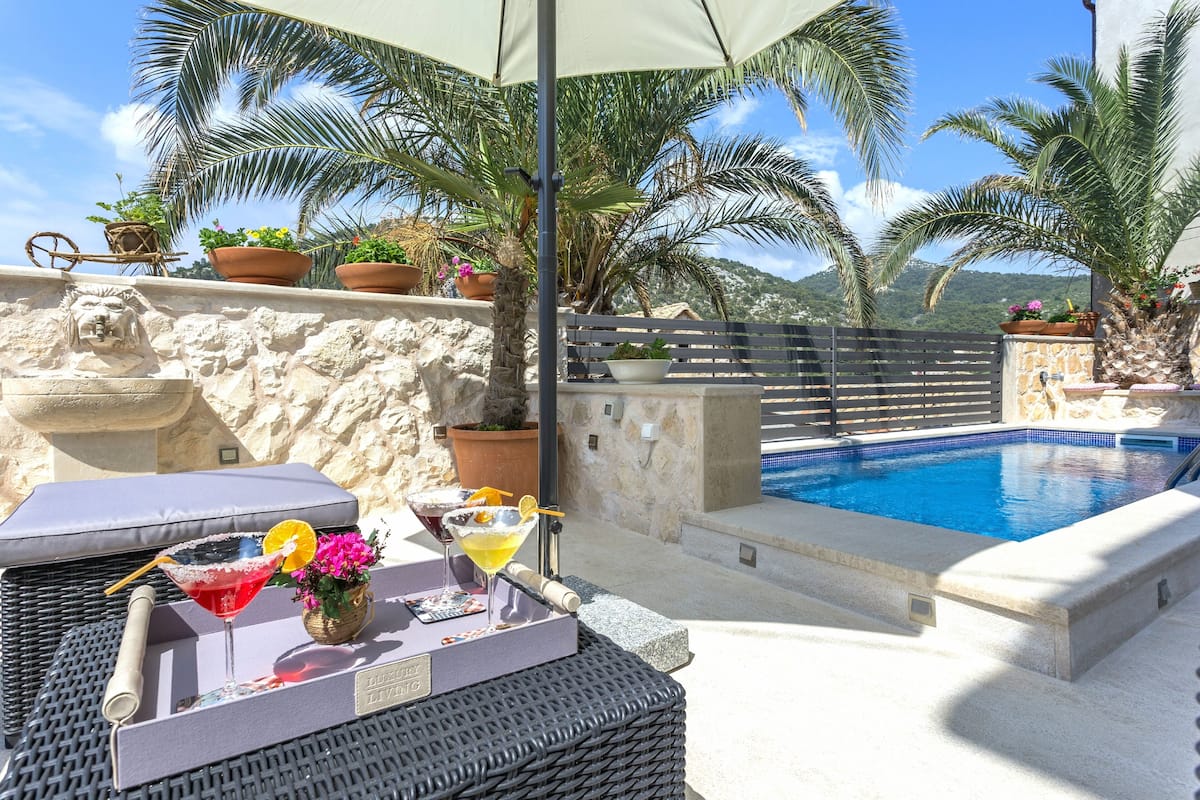 A poolside area with a lounge chair, a drink tray, and potted plants.