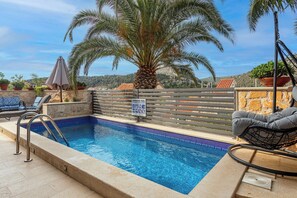 A swimming pool with a sign, lounge chairs, a palm tree, and a view of the hills. - Villa Capitis in the Centre - Private Pool Villa & Balcony Apartment with Amazing view (No Pool) (Hvar)