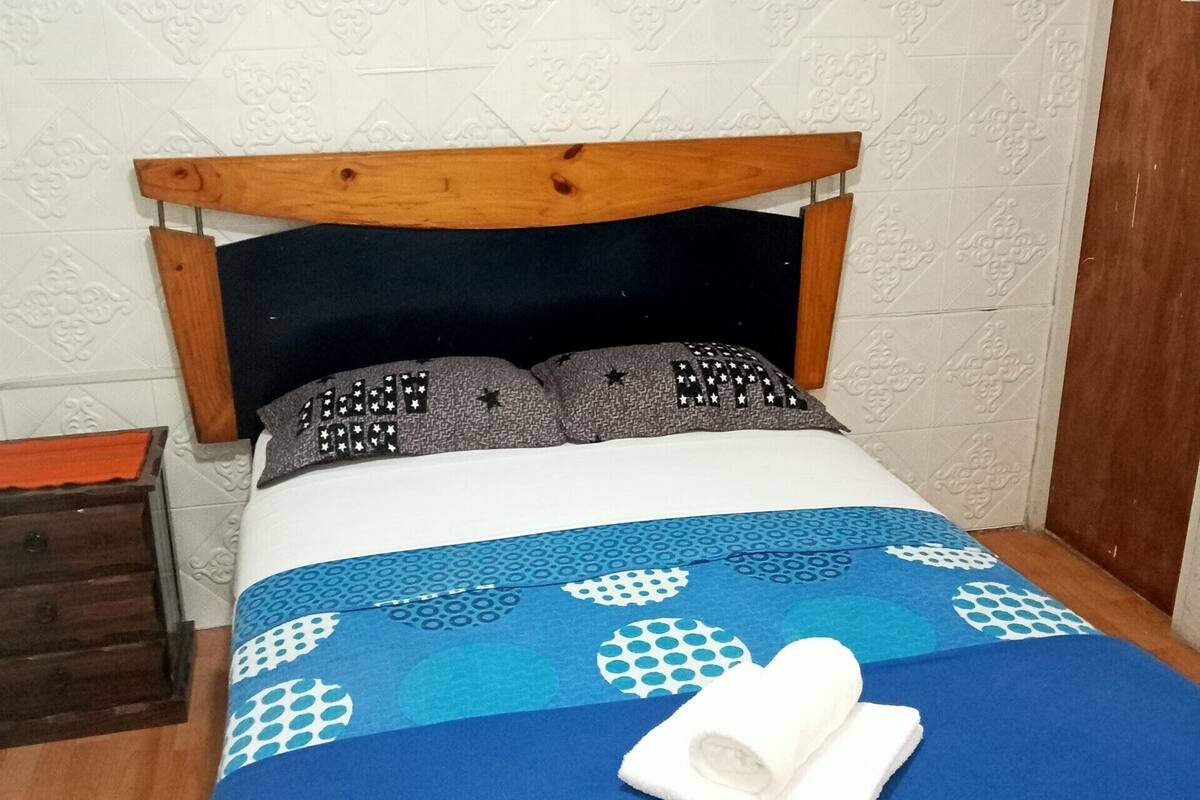 Ein ordentlich bezogenes Bett mit einer blau-weißen Bettdecke, einem hölzernen Kopfteil und einem gerahmten abstrakten Gemälde darüber.