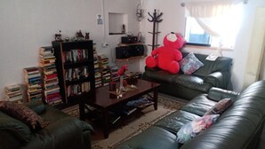 A living room with a leather sofa, a bookshelf, a coffee table, and a large red teddy bear. - HOSPEDERIA Calle 5 (Callao)