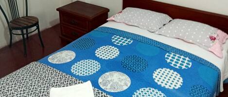 Un dormitorio con cama, una silla, una mesita de noche, un cuadro en la pared y un cartel de Wi-Fi.