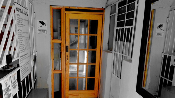 A hotel room with a wooden door, a window with bars, and various signs indicating amenities like breakfast hours and exchange services. - HOSPEDERIA Calle 5 (Callao)