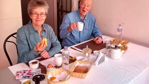 Two people seated at a table with breakfast items, including bread, eggs, and a teapot. - HOSPEDERIA Calle 5 (Callao)