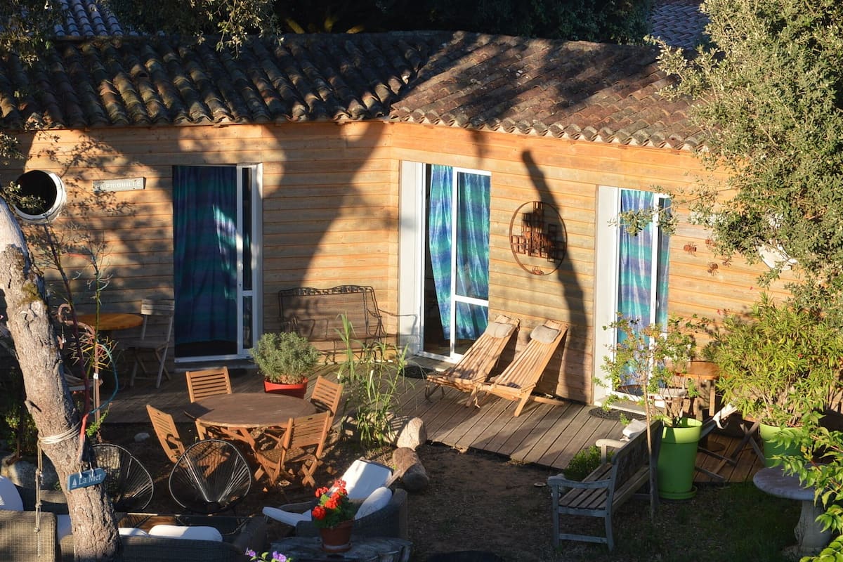 Uma cabana de madeira com um alpendre, mobiliário de exterior e um pequeno jardim.