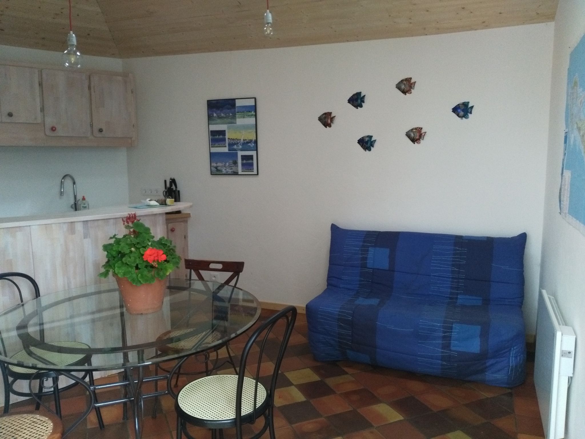 Un comedor con mesa de vidrio, sillas, una planta en maceta, un sofá y una pared decorada con peces.