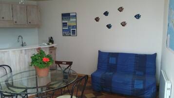 Un comedor con mesa de vidrio, sillas, una planta en maceta, un sofá y una pared decorada con peces.