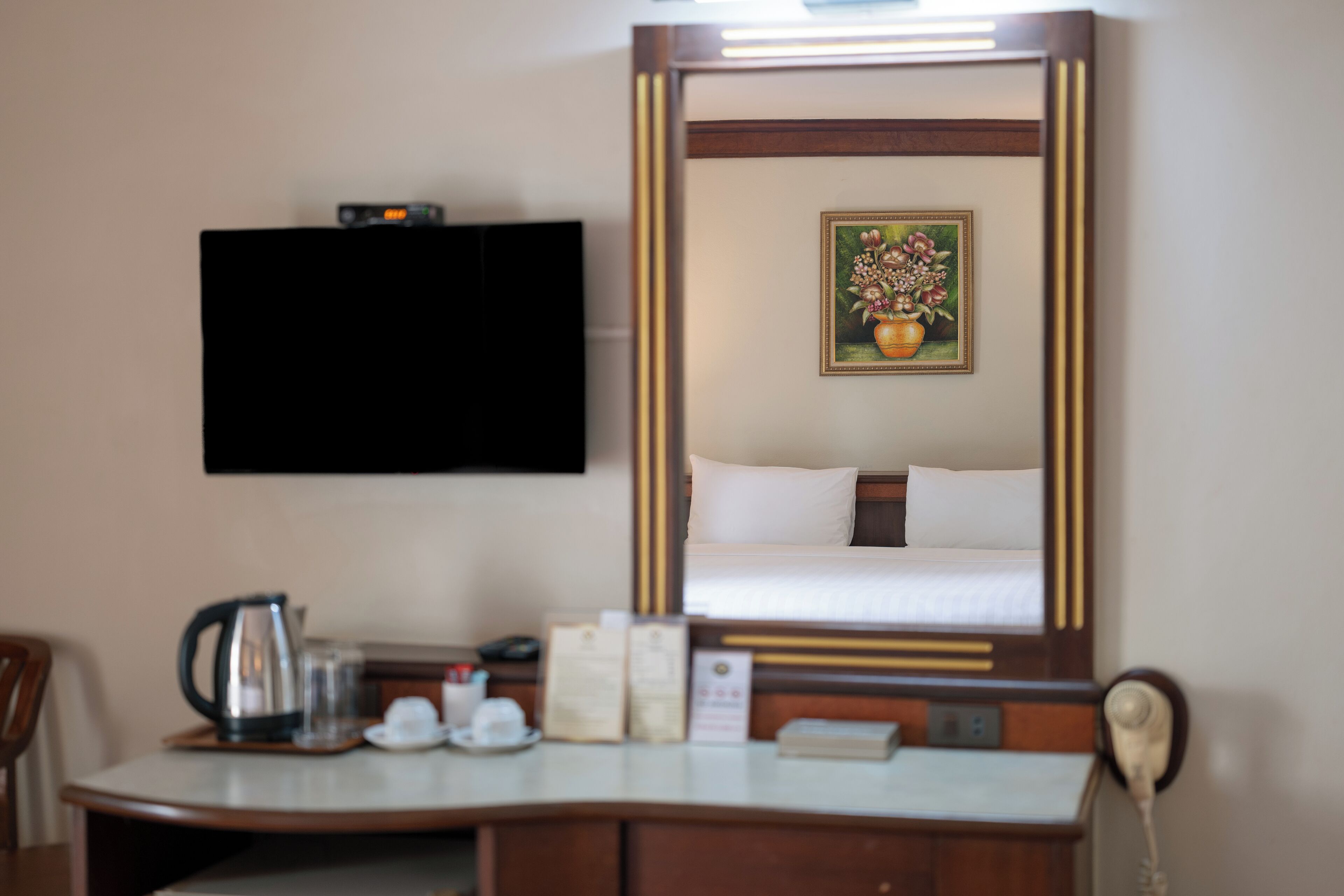 Una habitación de hotel con una cama, un escritorio con teléfono, una cafetera y un cuadro en la pared.