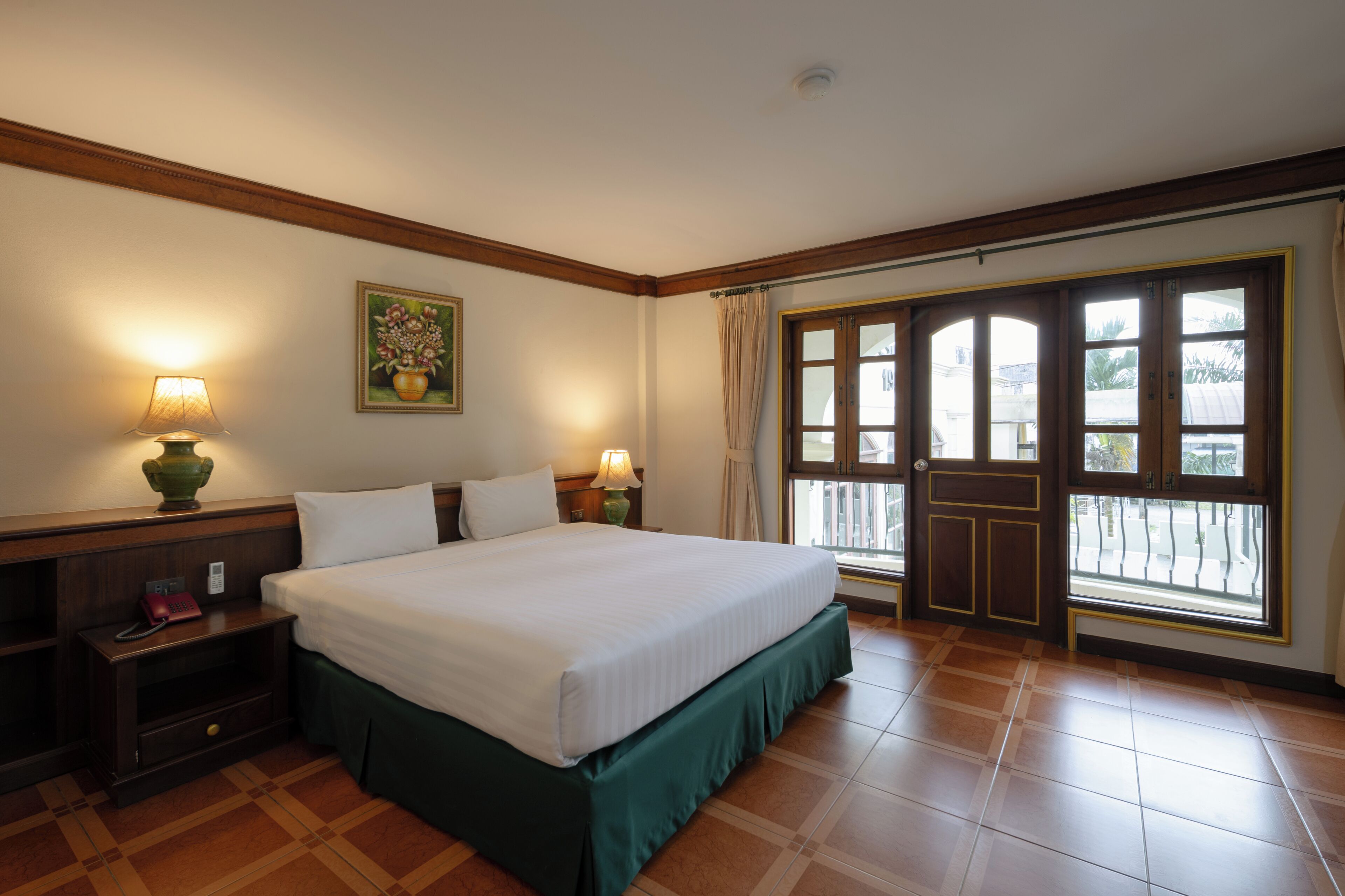 A hotel room with a large bed, two bedside tables with lamps, a nightstand, a window with curtains, and a door with a view.