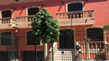Un edificio de fachada roja, un balcón con barandilla y un árbol en primer plano.