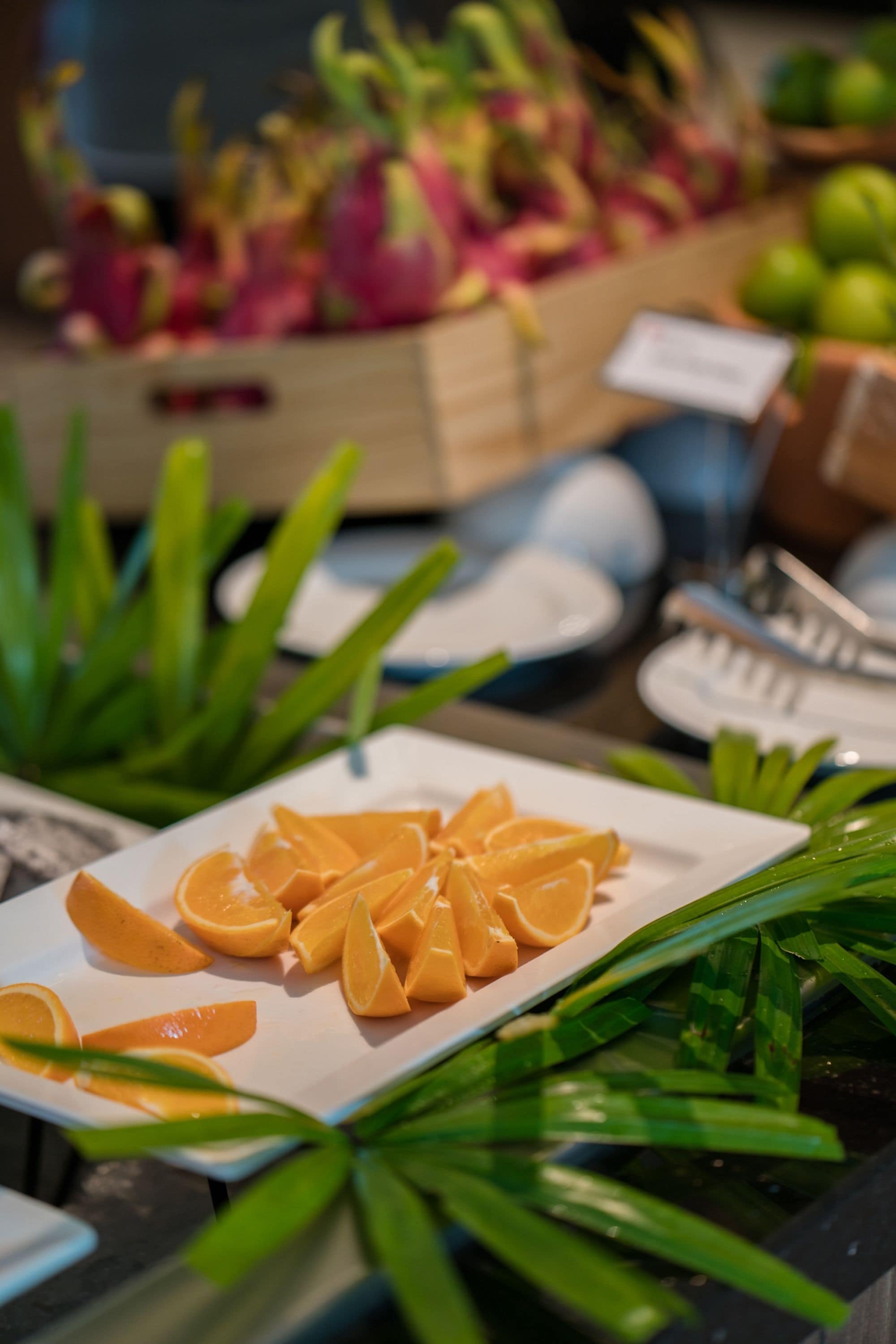 Un bufé con frutas y verduras cortadas, incluyendo naranjas y hojas verdes.