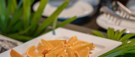 Un bufé con frutas y verduras cortadas, incluyendo naranjas y hojas verdes.