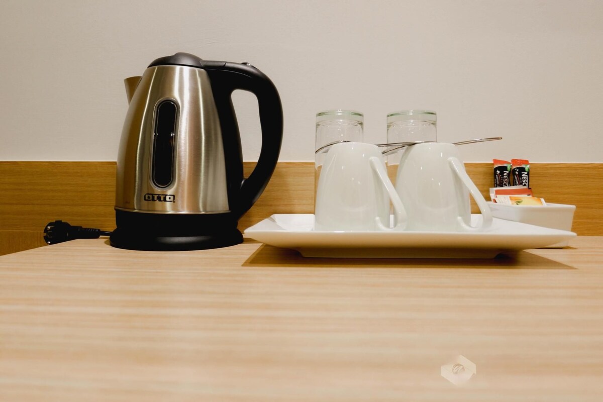 Un área de cocina con un hervidor, dos tazas y un plato con salsas y aderezos.