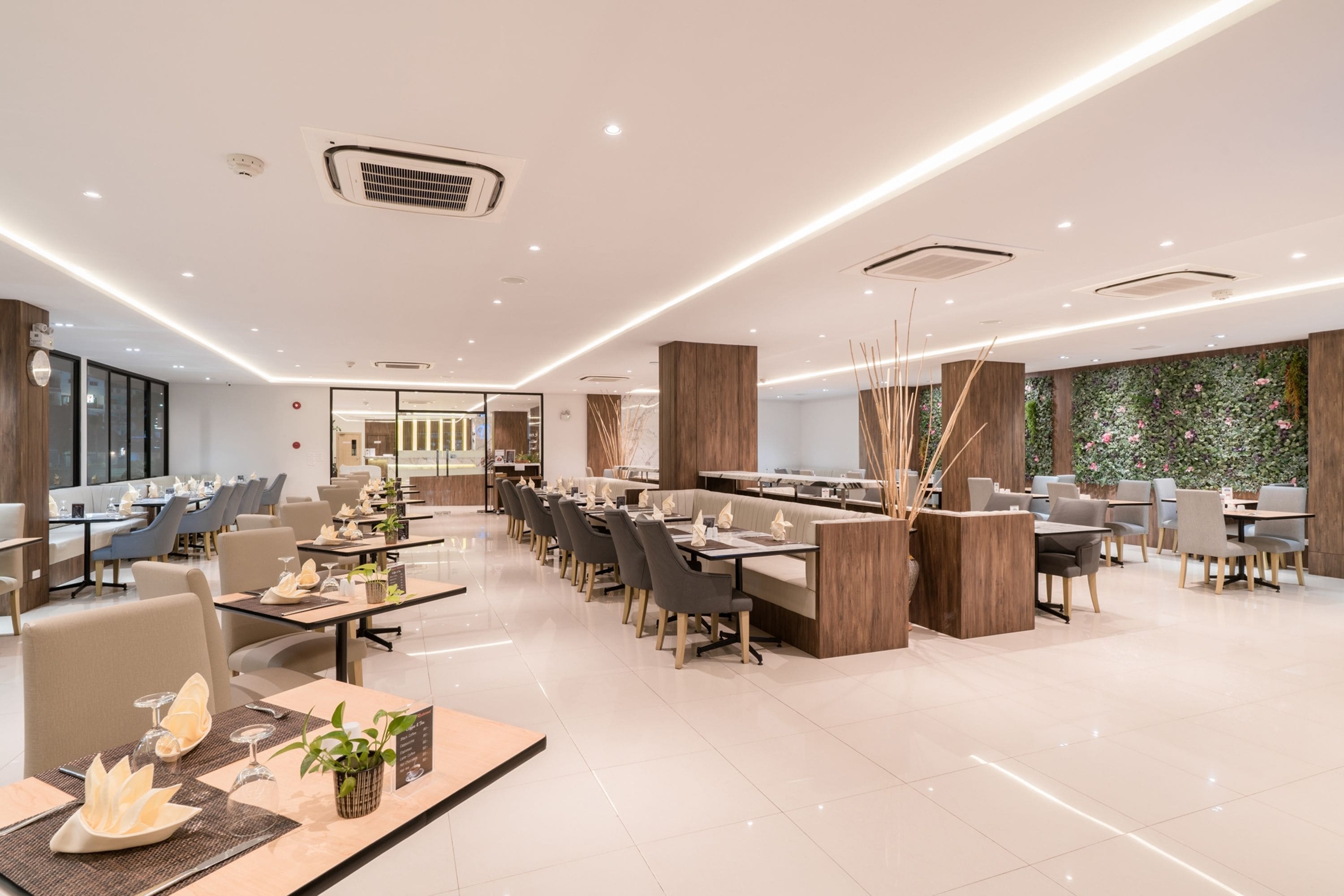 Un restaurante moderno con una barra larga, varias zonas de estar y una pared decorativa con plantas.