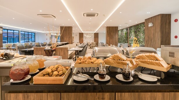 A buffet area with various food items and beverages, wooden paneling, and a modern interior design. - New Square Patong Hotel (Patong)