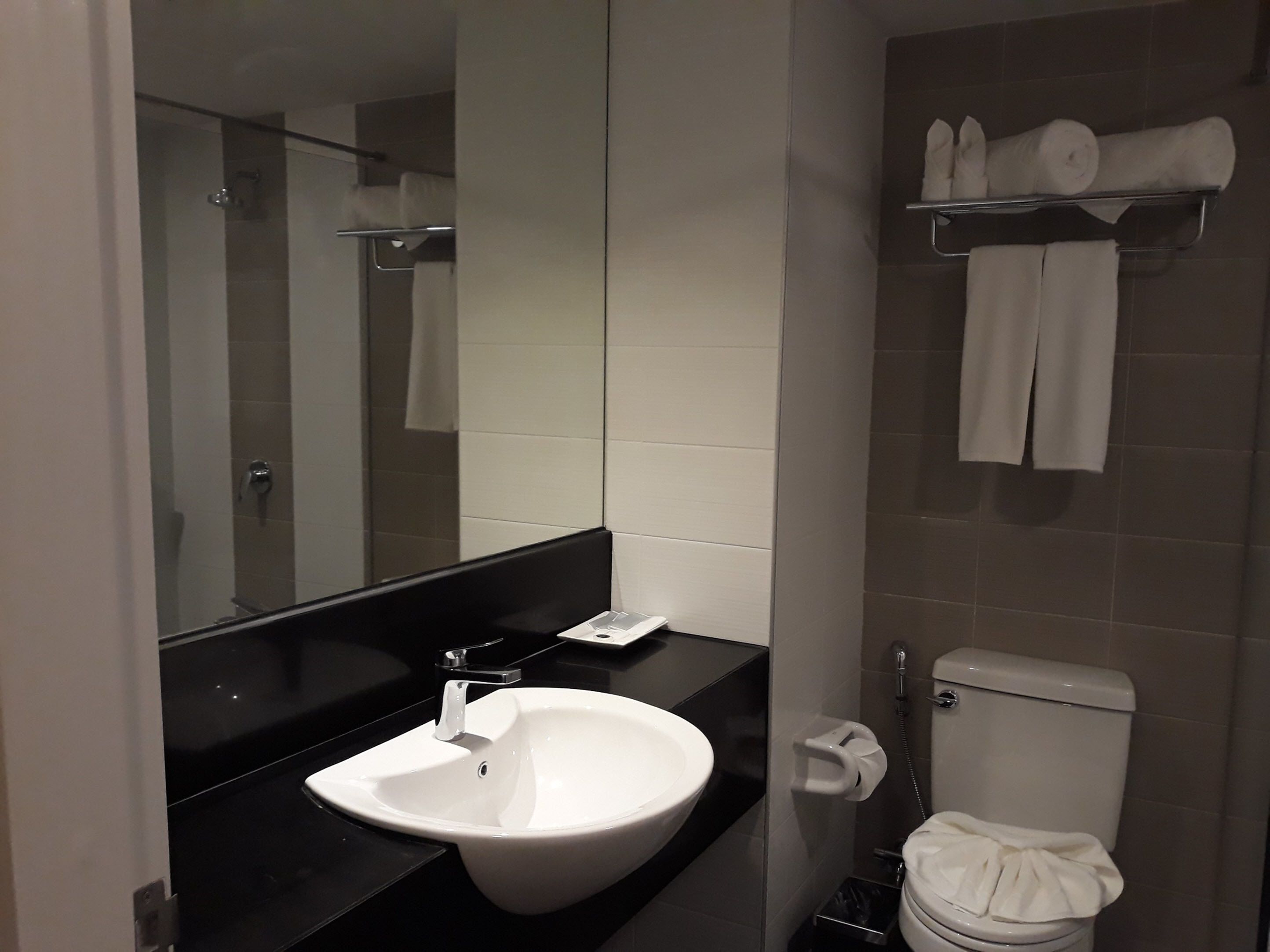 A modern bathroom with a white sink, a mirror, a toilet, and a towel rack.