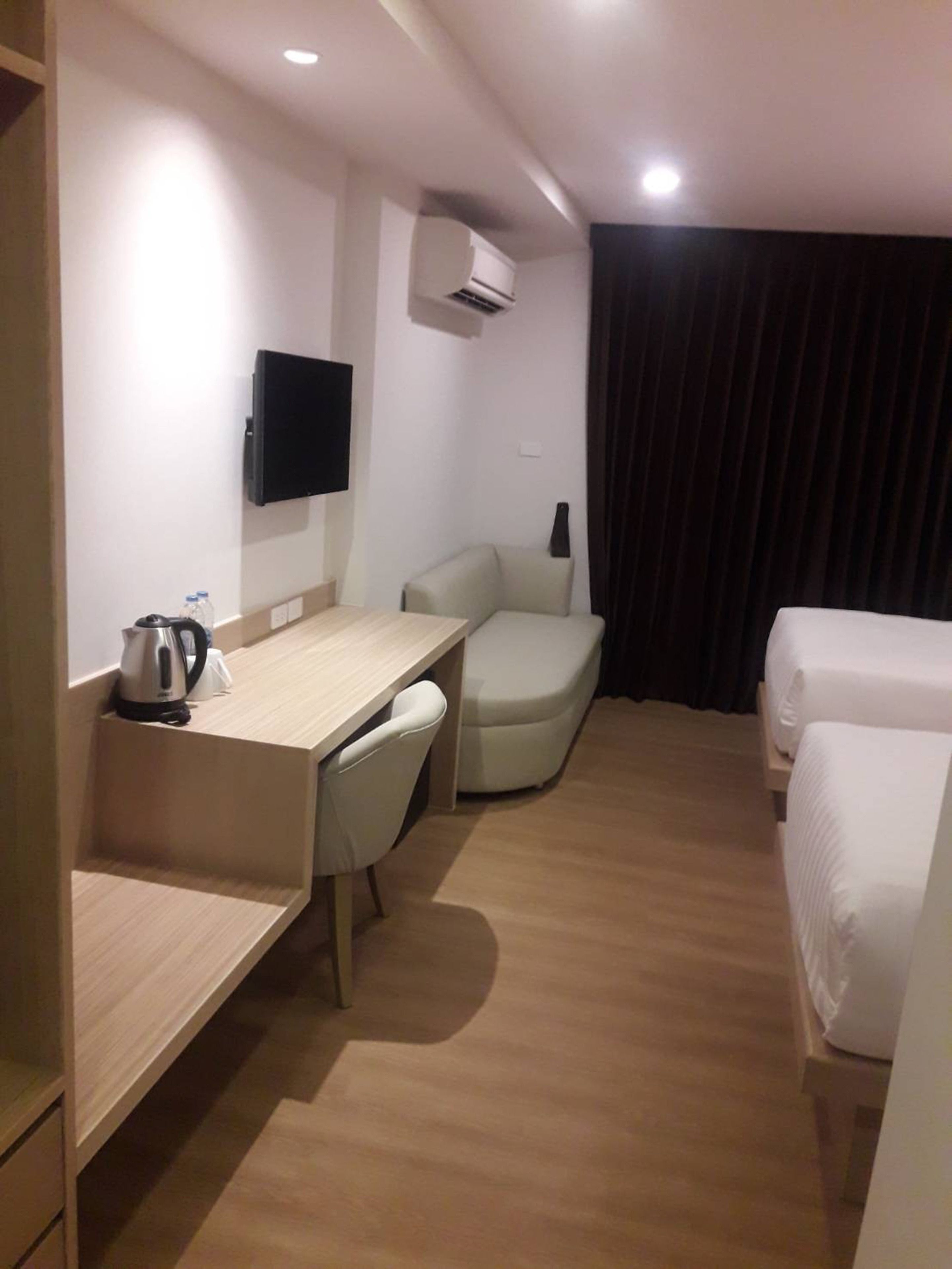 A hotel room with a desk, chair, two beds, a TV, and an air conditioner.