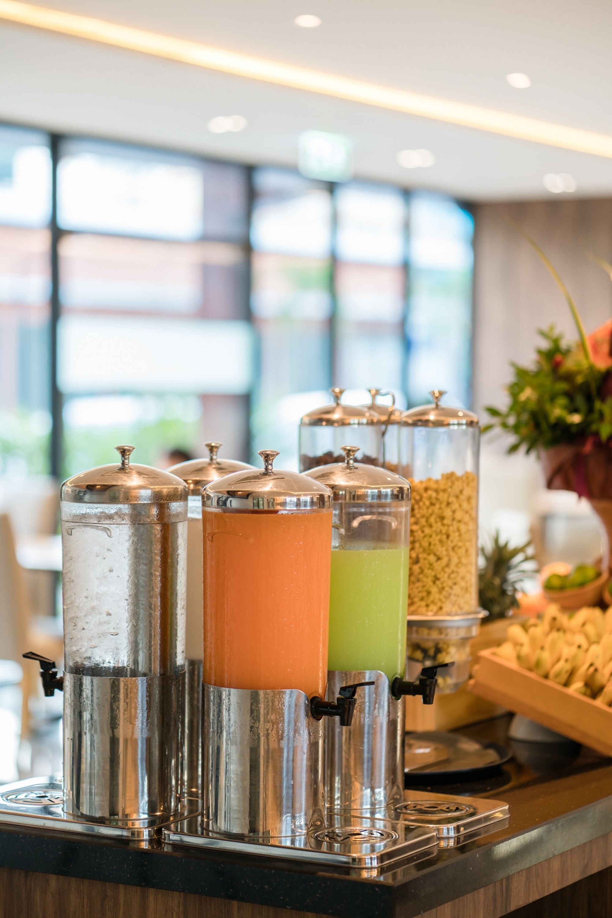 Un dispensador de bebidas con varios recipientes, un frutero y una planta en un hotel.