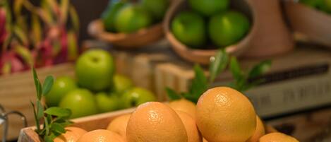 Una caja de madera llena de naranjas, un tazón de manzanas verdes y una planta en maceta con un lazo rojo.