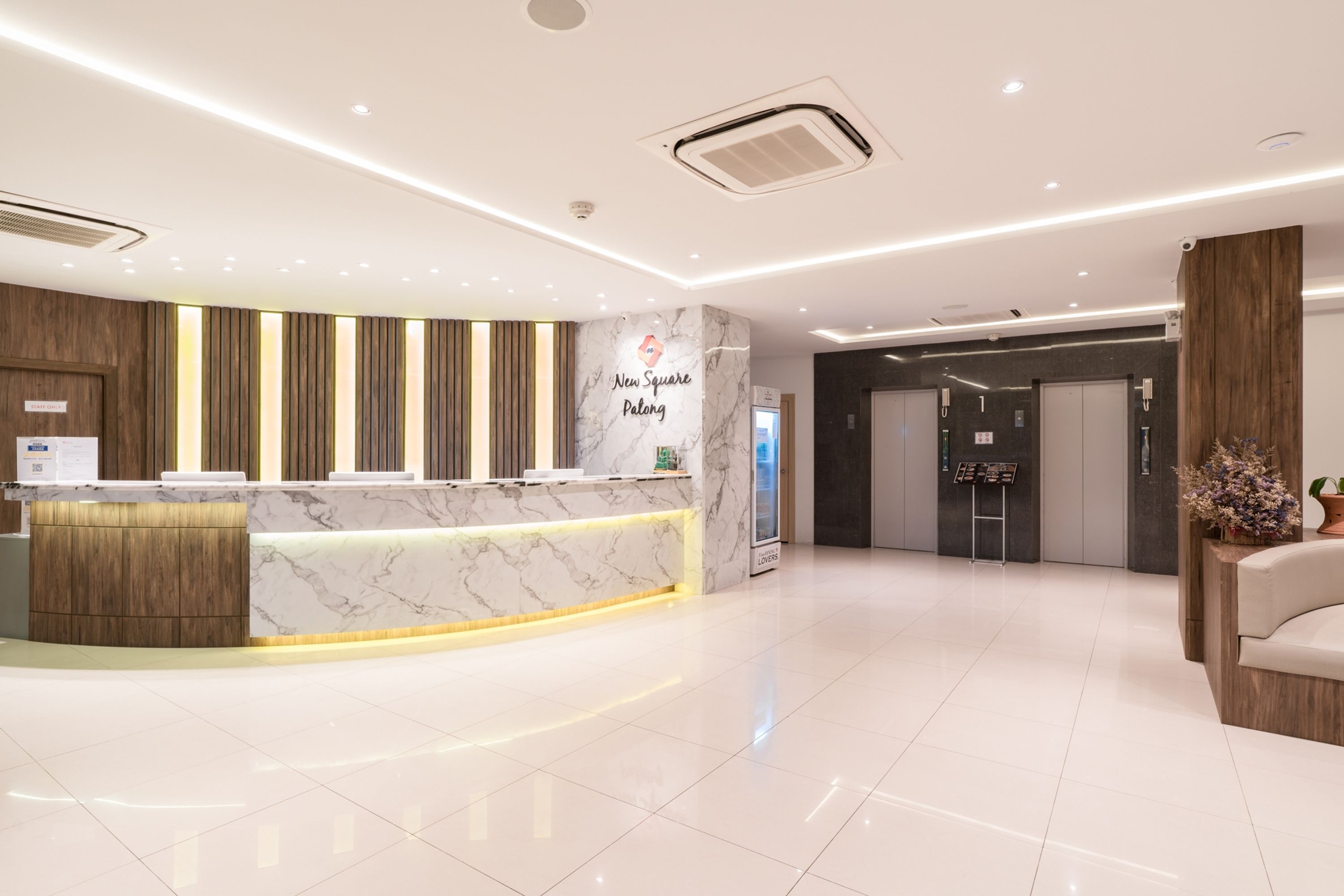 A modern hotel reception area with a marble counter, wooden accents, and a sign reading "New Square Palong".