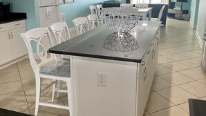 A modern kitchen with white cabinetry, a granite countertop, and a dining area with white chairs. - 2000sq ft Villa 401, Ocean View steps to the beach, small pool hot tub 4 king bd (North Myrtle Beach)