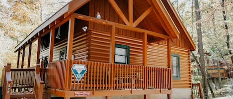 A wooden cabin with a porch, a sign indicating it is part of the Woodland Dream's collection, and a number '520' on the railing.
