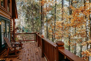 A wooden deck with chairs, surrounded by a forest with autumn foliage. - Cozy Log Cabin Near Dollywood | Hot Tub, Game Loft & Free Attraction Tickets (Sevierville)
