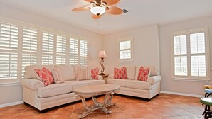 A living room with a beige sectional sofa, a round coffee table, and a ceiling fan. - Sunseeker - Xanadu by Coastal Dreamin (Santa Rosa Beach)