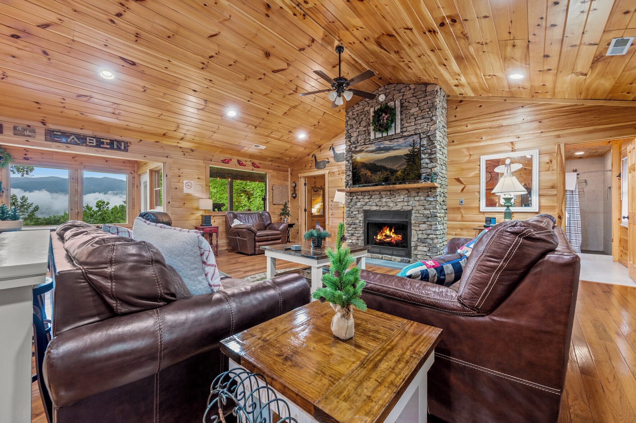 A cabin interior with leather sofas, a stone fireplace, and a ceiling fan.