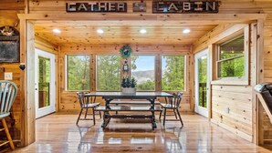 Ein Interieur einer Holzhütte mit einem Holzespeisetisch, Bänken und großen Fenstern mit Blick auf den Wald.