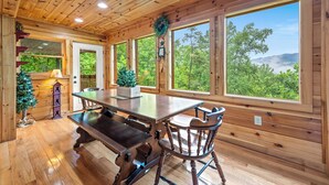 Ein Holzblockhaus-Interieur mit Esstisch, Stühlen und großen Fenstern mit Blick auf den Wald.