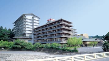 A hotel with multiple floors, traditional Japanese architectural style, and a parking area in front.