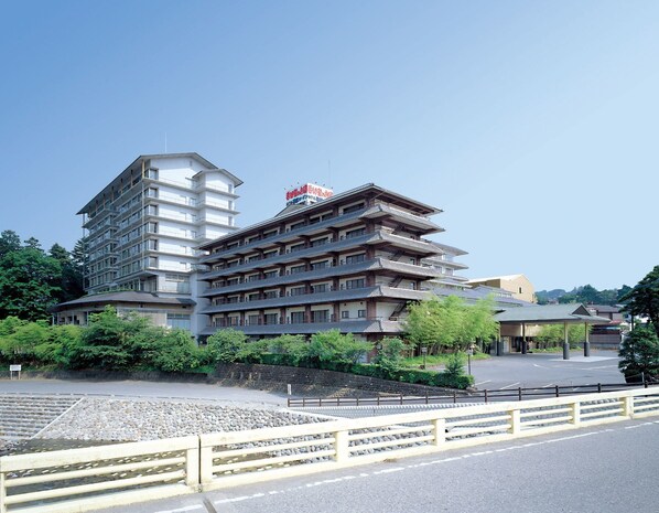 A hotel with multiple floors, traditional Japanese architectural style, and a parking area in front.