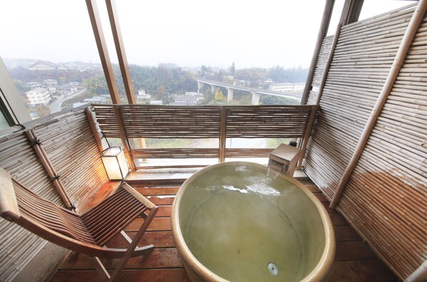 A wooden deck with a hot tub and seating area, overlooking a bridge and cityscape.
