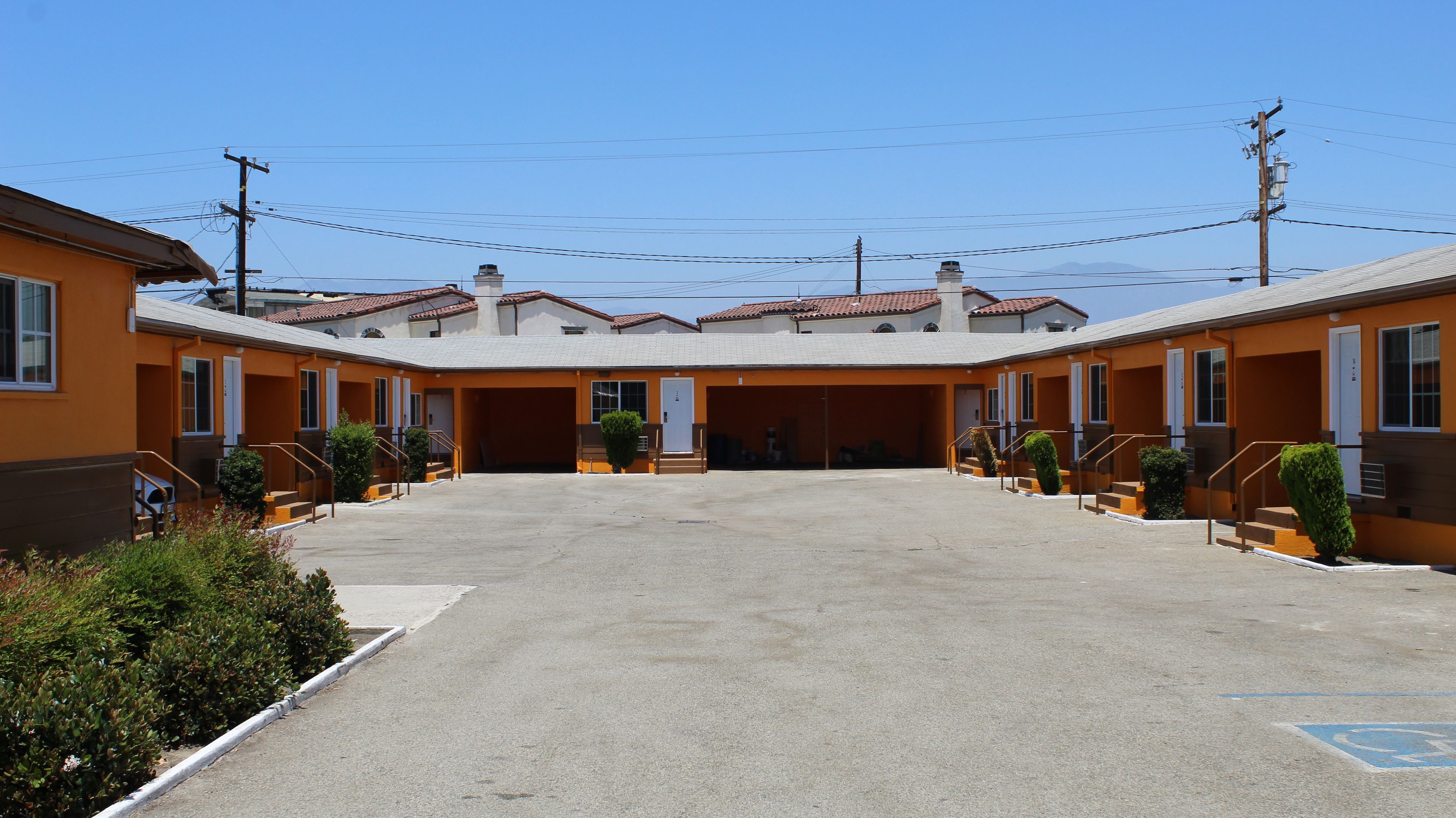 A row of orange motel buildings with a central parking area and a clear blue sky.