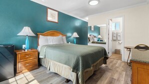 Une chambre à coucher comprenant un lit, deux tables de chevet avec des lampes, une commode et une porte donnant sur une salle de bain.