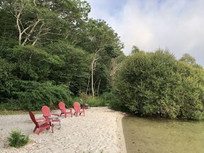 Une plage avec des chaises rouges et une table, entourée d’une végétation luxuriante et d’arbres.
