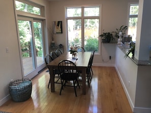 Un espace repas avec une table et des chaises en bois, de grandes fenêtres et une vue sur l’extérieur.