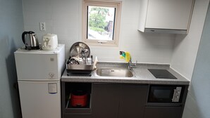 Een compacte keuken met een ingebouwde vaatwasser, een kleine koelkast, een spoelbak en een raam boven de spoelbak.