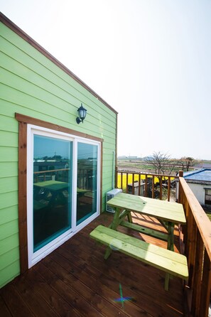 A wooden deck with a picnic table and benches, a sliding glass door, and a view of a rural landscape.